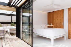 Un dormitorio moderno con una puerta de vidrio que da a un balcón, una cama blanca y un armario de madera.