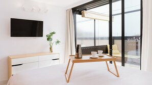 Quarto de hotel moderno com cama, mesa de cabeceira, televisão de tela plana, planta em vaso e varanda com vista.