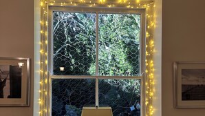 Une fenêtre avec un cadre blanc et des guirlandes lumineuses, un radiateur en dessous, et deux petites statues de chaque côté.