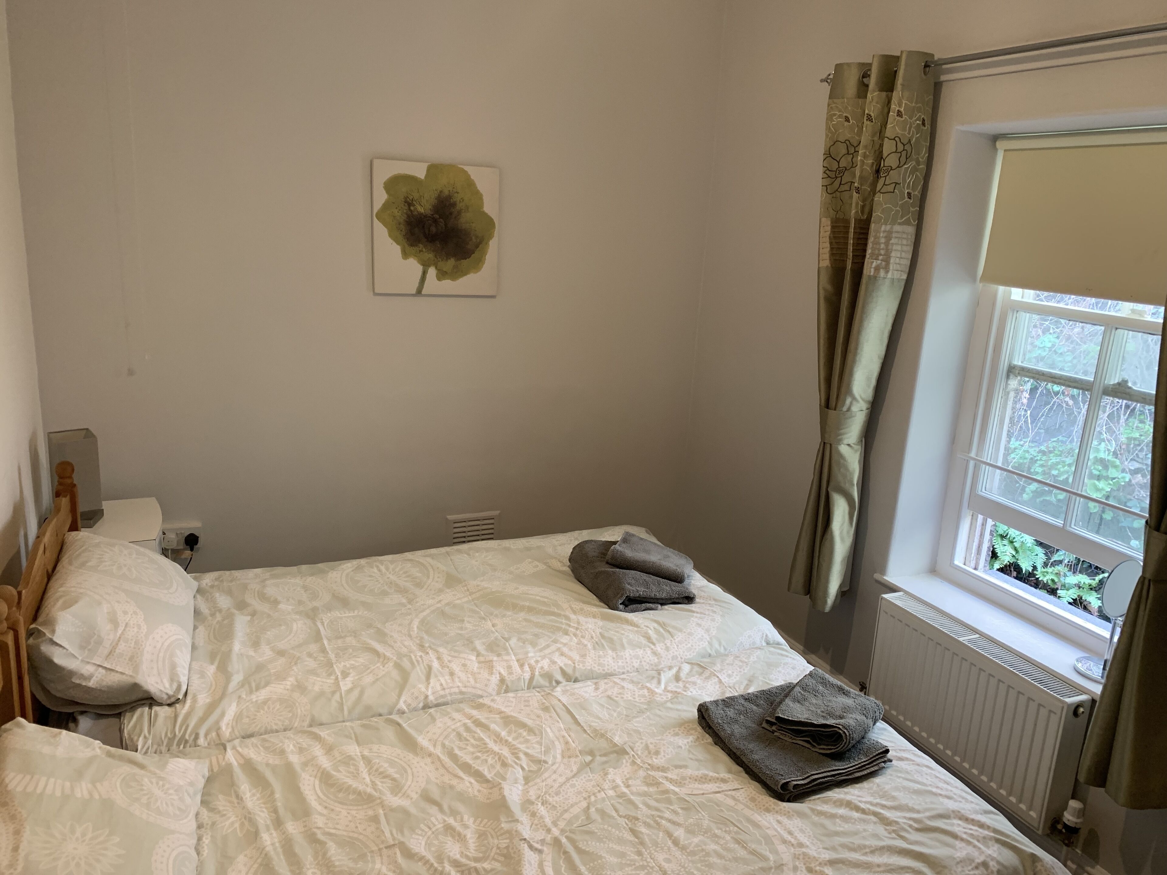 A bedroom with a bed, a radiator, a window with curtains, and a wall-mounted artwork.