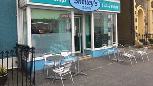 Une devanture de magasin avec une enseigne indiquant « Shelley's Fish & Chips » et des places assises à l’extérieur, avec des chaises et des tables en métal.