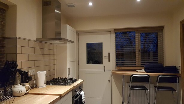 A compact kitchen with a gas stove, a coffee maker, and a window with blinds. - Welcome to Tuolumne Cottage (Denbigh)
