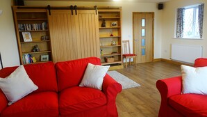 A living room with a red sofa set, a wooden bookshelf, and a sliding door. - Welcome to Tuolumne Cottage (Denbigh)