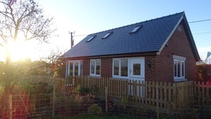 A brick house with a sloped roof, white-framed windows, and a wooden fence. - Welcome to Tuolumne Cottage (Denbigh)