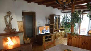 A cozy living room with a fireplace, wooden furniture, and a television displaying a news broadcast.