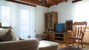 A living room with a sofa, a wooden rocking chair, a television, and a cabinet.