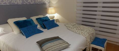 A neatly made bed with multiple pillows, a bedside lamp, and a small stool.