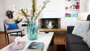 Ein Wohnzimmer mit einem weißen Couchtisch, einer blauen Vase mit Blumen, einem Kamin, einem grauen Sofa und einer Bücherwand mit Dekorationsobjekten.