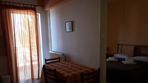 A room with a dining table, chairs, a bed, and a radiator. - Katerina Apartments ,( 2 ) One-Bedroom Apartment with Balcony (Kalamata)