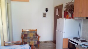 A compact kitchen with a refrigerator, stove, and a dining area with a table and chairs. - Katerina Apartments ,( 2 ) One-Bedroom Apartment with Balcony (Kalamata)