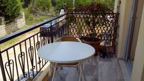 A balcony with a white table and wicker chairs, a potted plant, and a metal fence. - Katerina Apartments ,( 2 ) One-Bedroom Apartment with Balcony (Kalamata)