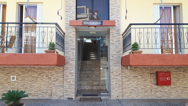 A hotel entrance with a sign reading "KATERINA," a staircase leading inside, and a fire hose with a water hose visible on the wall. - Katerina Apartments ,( 2 ) One-Bedroom Apartment with Balcony (Kalamata)