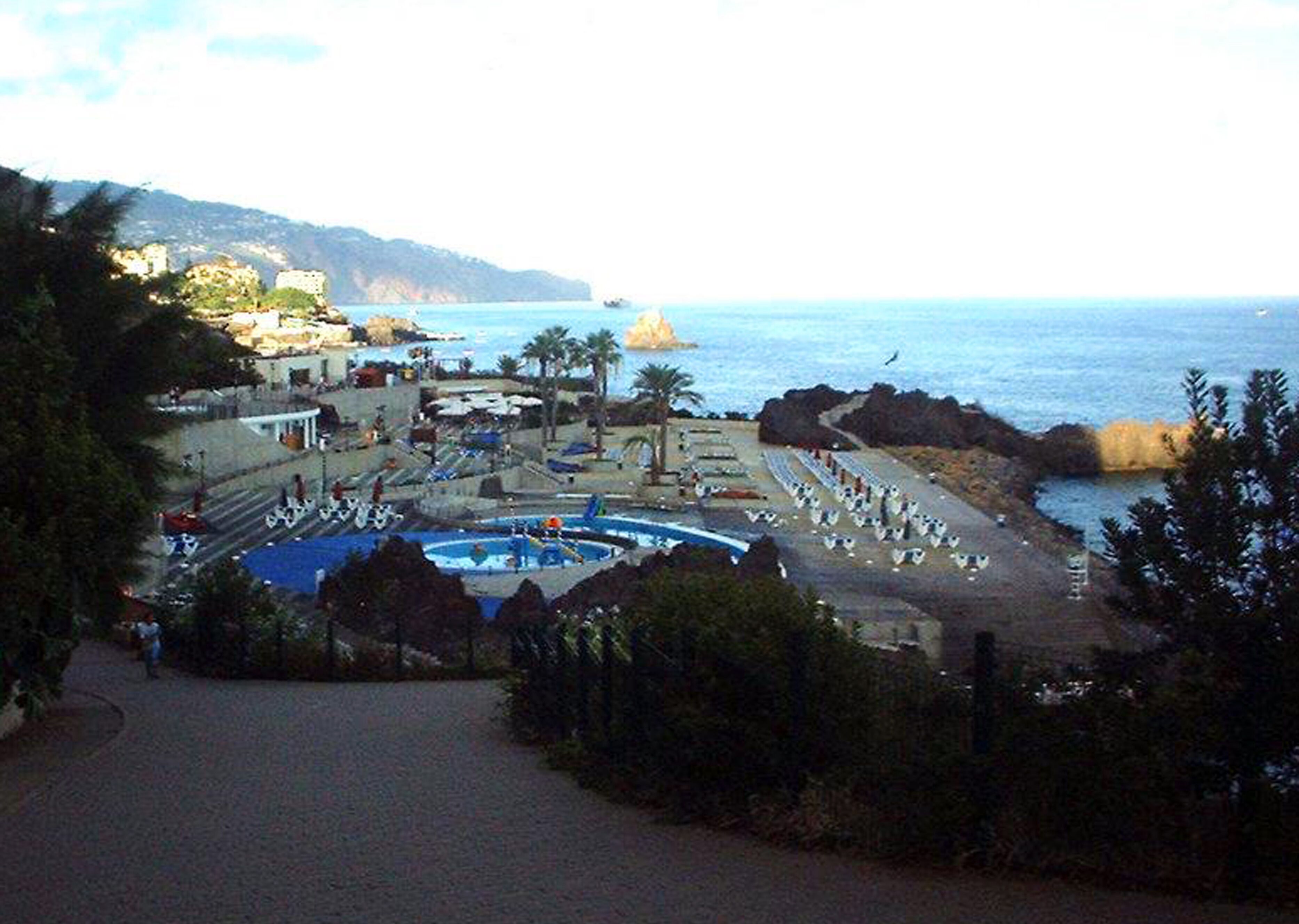 A coastal resort with a swimming pool, beach chairs, and umbrellas.
