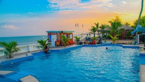 A swimming pool with a view of the ocean, a small pavilion, and palm trees. - Coconut Pointe Villa & Beach Resort (Prampram)