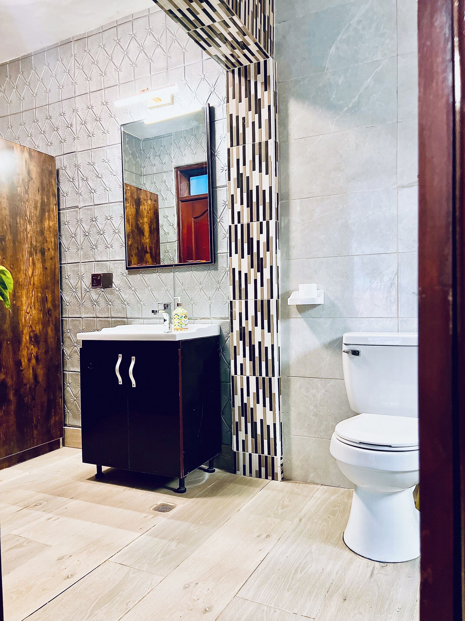A modern bathroom with a black vanity, a mirror, a toilet, and patterned tiles.