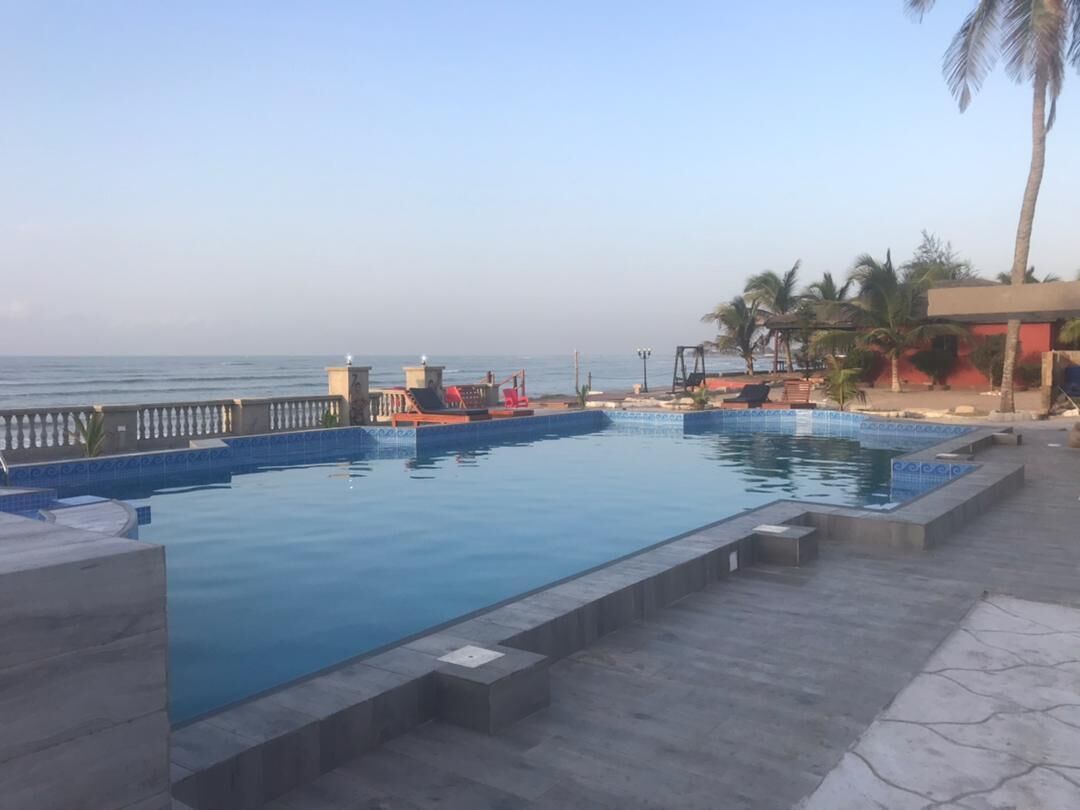 A swimming pool with a tiled deck, a palm tree, and a view of the sea.