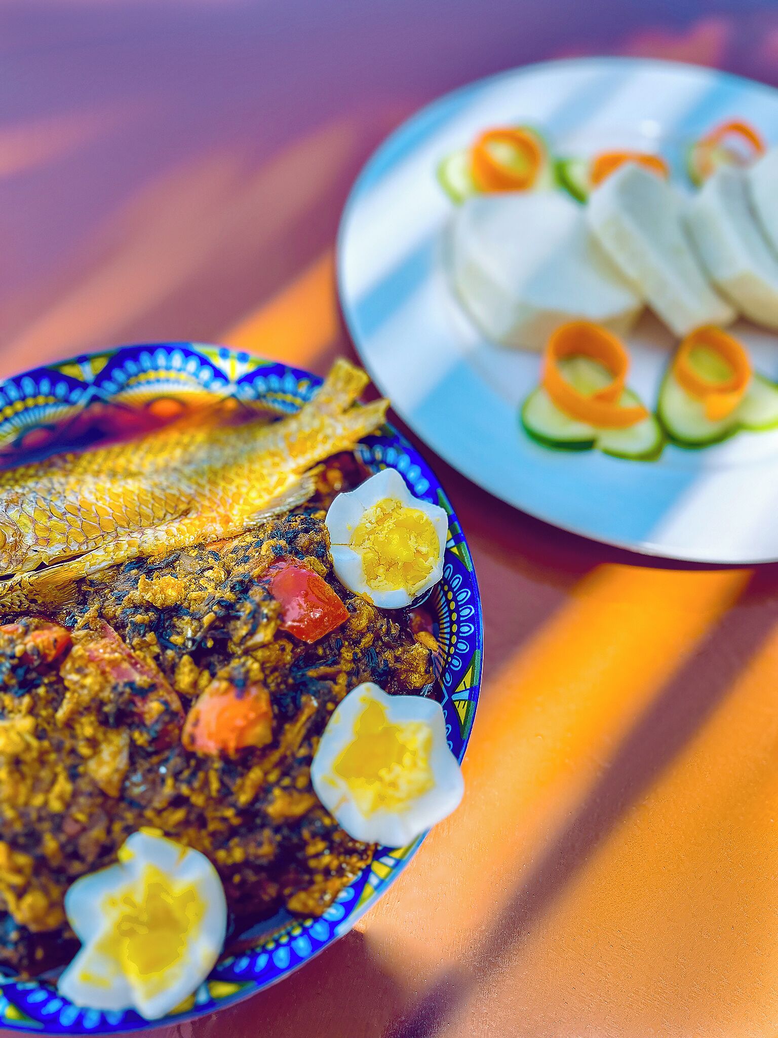 A plate of fish with vegetables and a boiled egg, and a plate of sliced cucumbers and carrots.