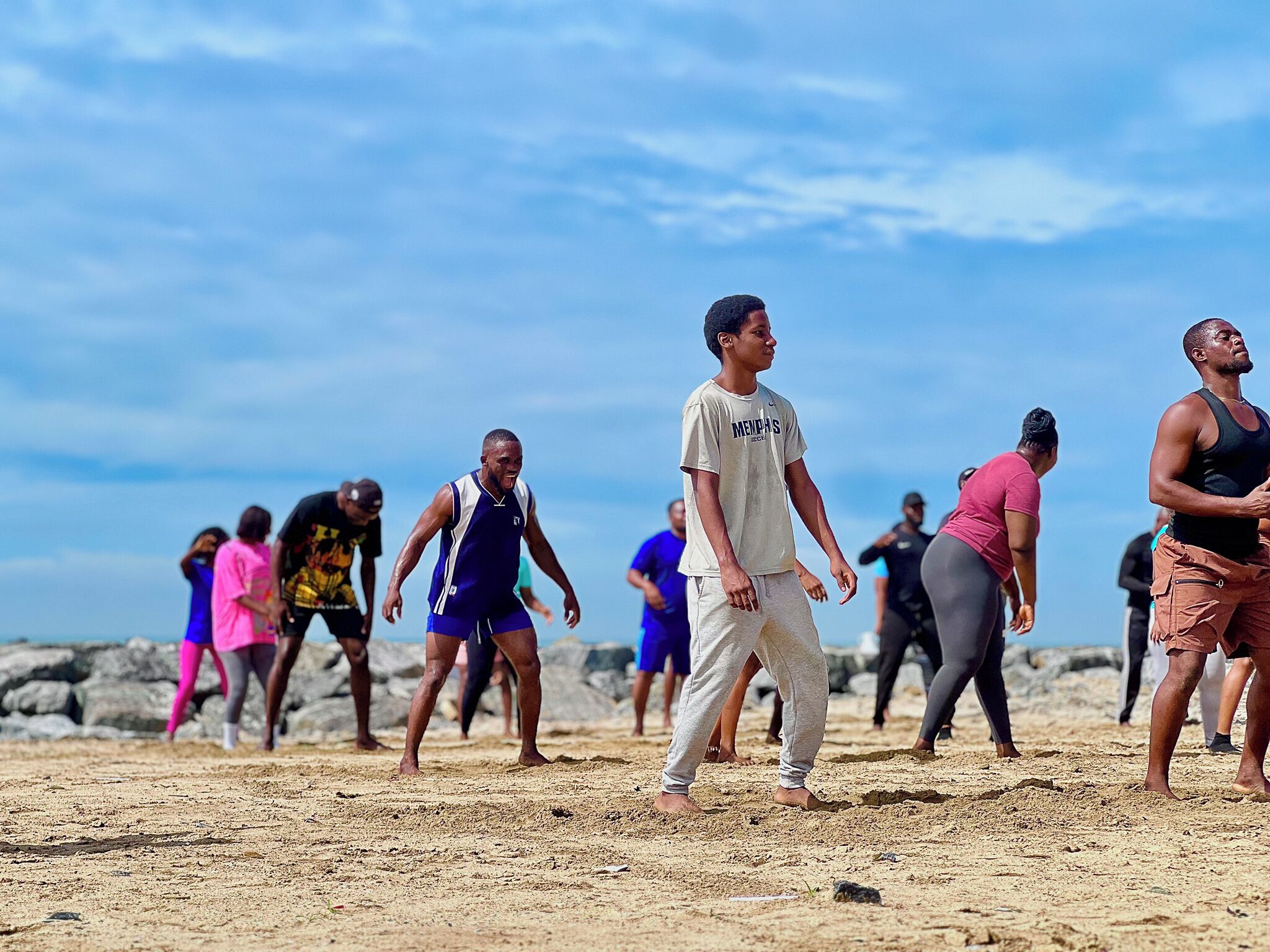 Un grupo de personas en una playa arenosa con terreno rocoso al fondo.