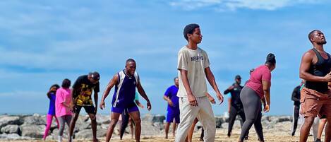 Un grupo de personas en una playa arenosa con terreno rocoso al fondo.
