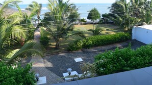 A view of a garden with palm trees, a pathway, and a view of the ocean. - Coconut Pointe Villa & Beach Resort (Prampram)