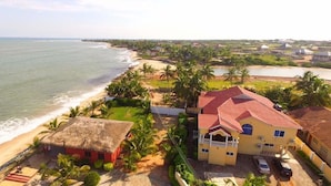 A coastal property with a beach, a thatched-roof structure, and a main building with a red roof. - Coconut Pointe Villa & Beach Resort (Prampram)