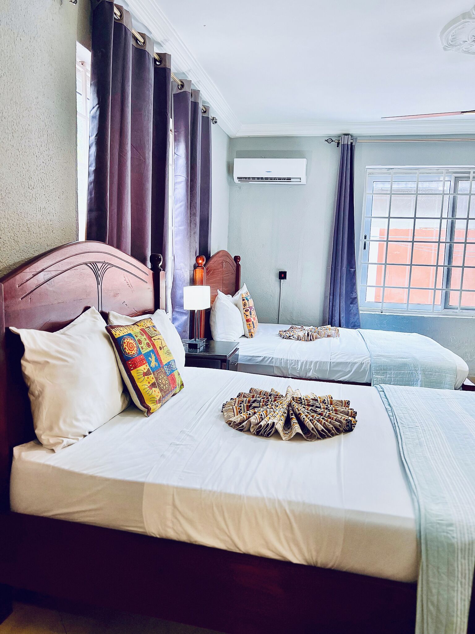 Habitación de hotel con dos camas, una mesita de noche, un equipo de aire acondicionado y una ventana con vistas a edificios.