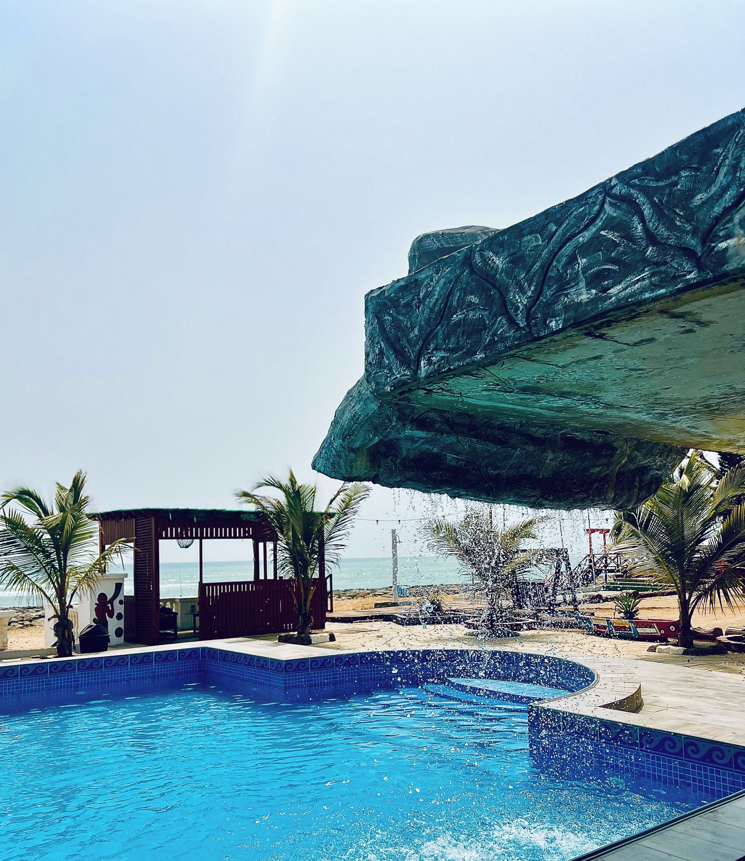 A swimming pool with a tropical setting, including palm trees and a beach in the background.