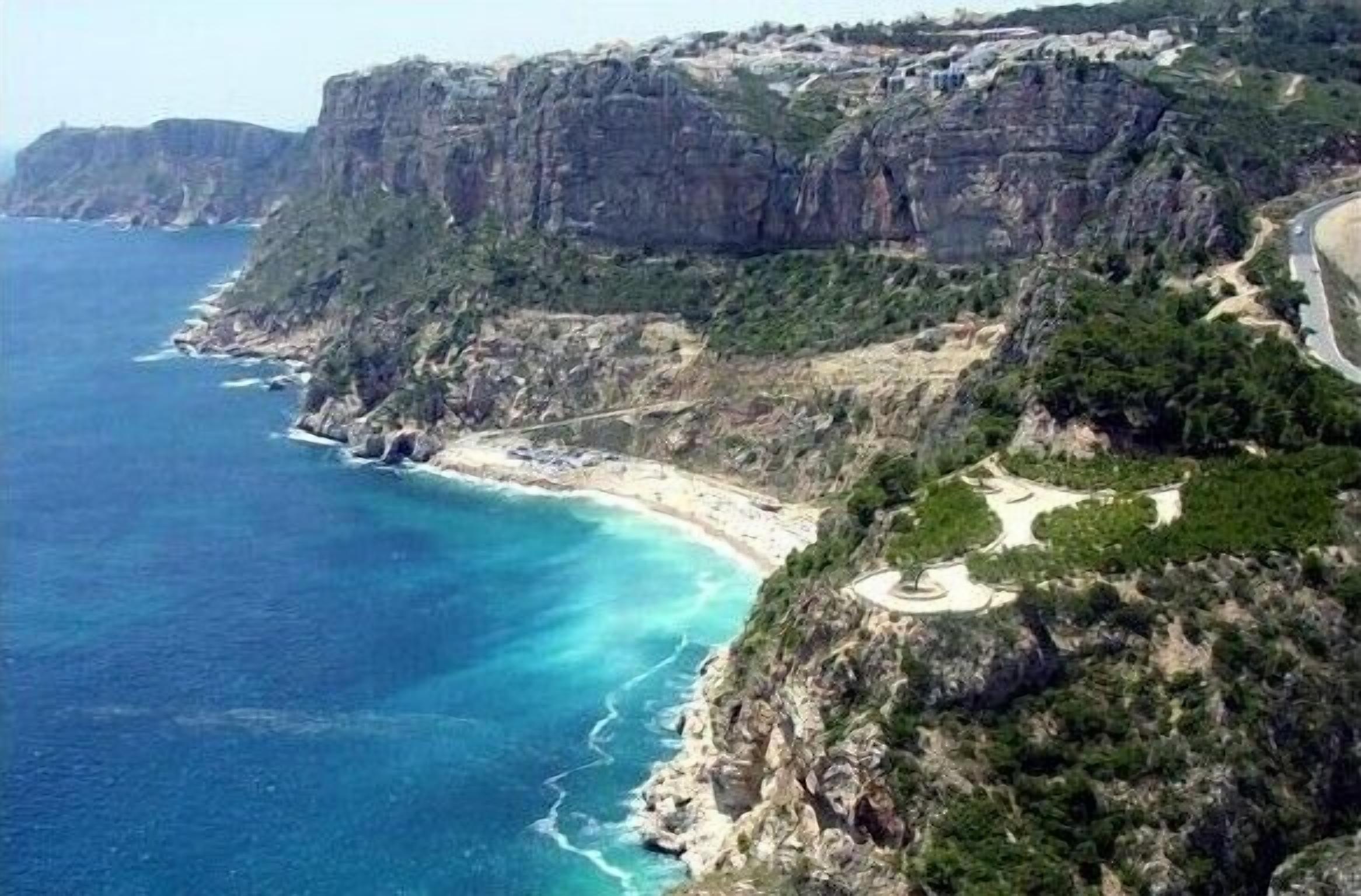 A coastal landscape with a winding road, cliffs, and a beach.