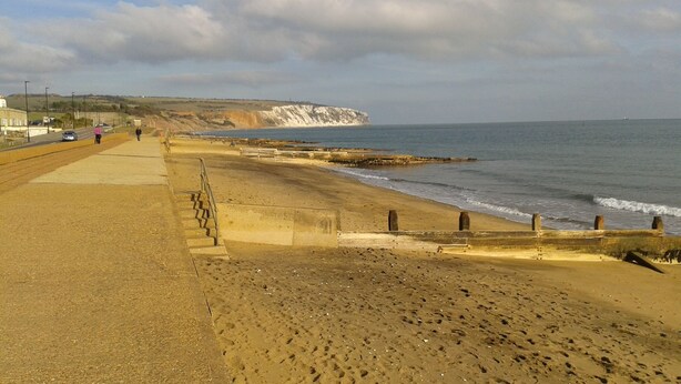 A coastal road with a sandy beach and cliffs in the background.