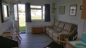 A cozy living room with a striped sofa, a wooden chest of drawers, a dining table with chairs, and a large window with curtains.