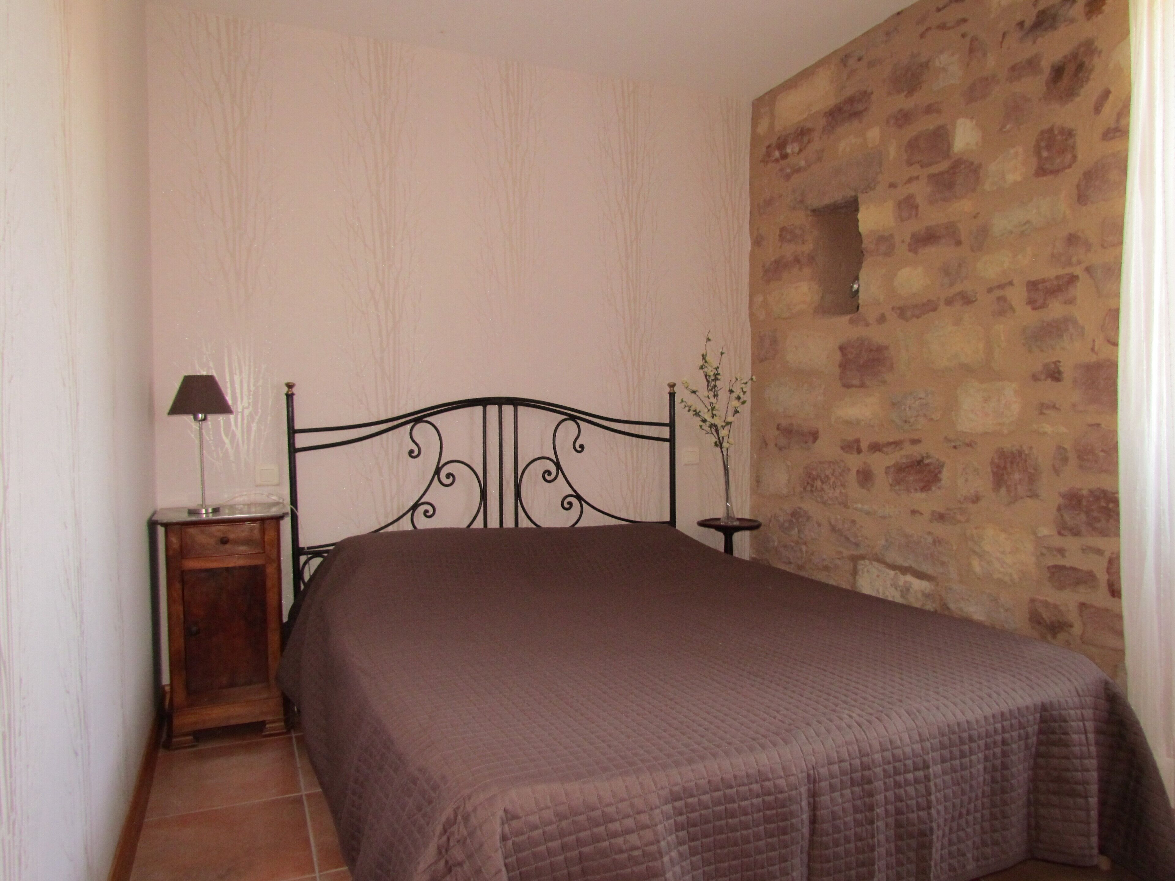 A bedroom with a bed, a nightstand, a lamp, and a vase with flowers.