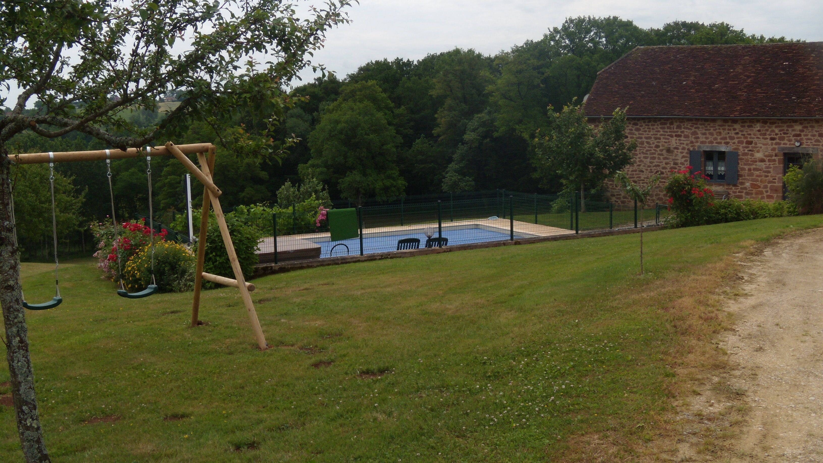 A grassy area with a swing set, a fenced pool, and a stone building.