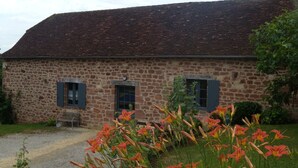 Un bâtiment en pierre avec un toit en pente, deux fenêtres avec volets et une allée gravillonnée.