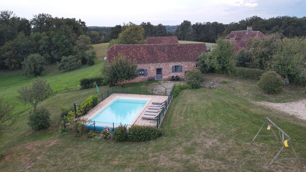 Une maison en pierre avec une piscine, entourée d’une pelouse et d’arbres.
