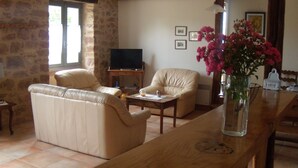 Un salon comprenant un canapé, deux fauteuils, une table basse et un téléviseur. On peut y voir un vase rempli de fleurs posé sur une table en bois.