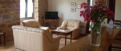 A living room with a sofa, two armchairs, a coffee table, and a TV. There is a vase with flowers on a wooden table.