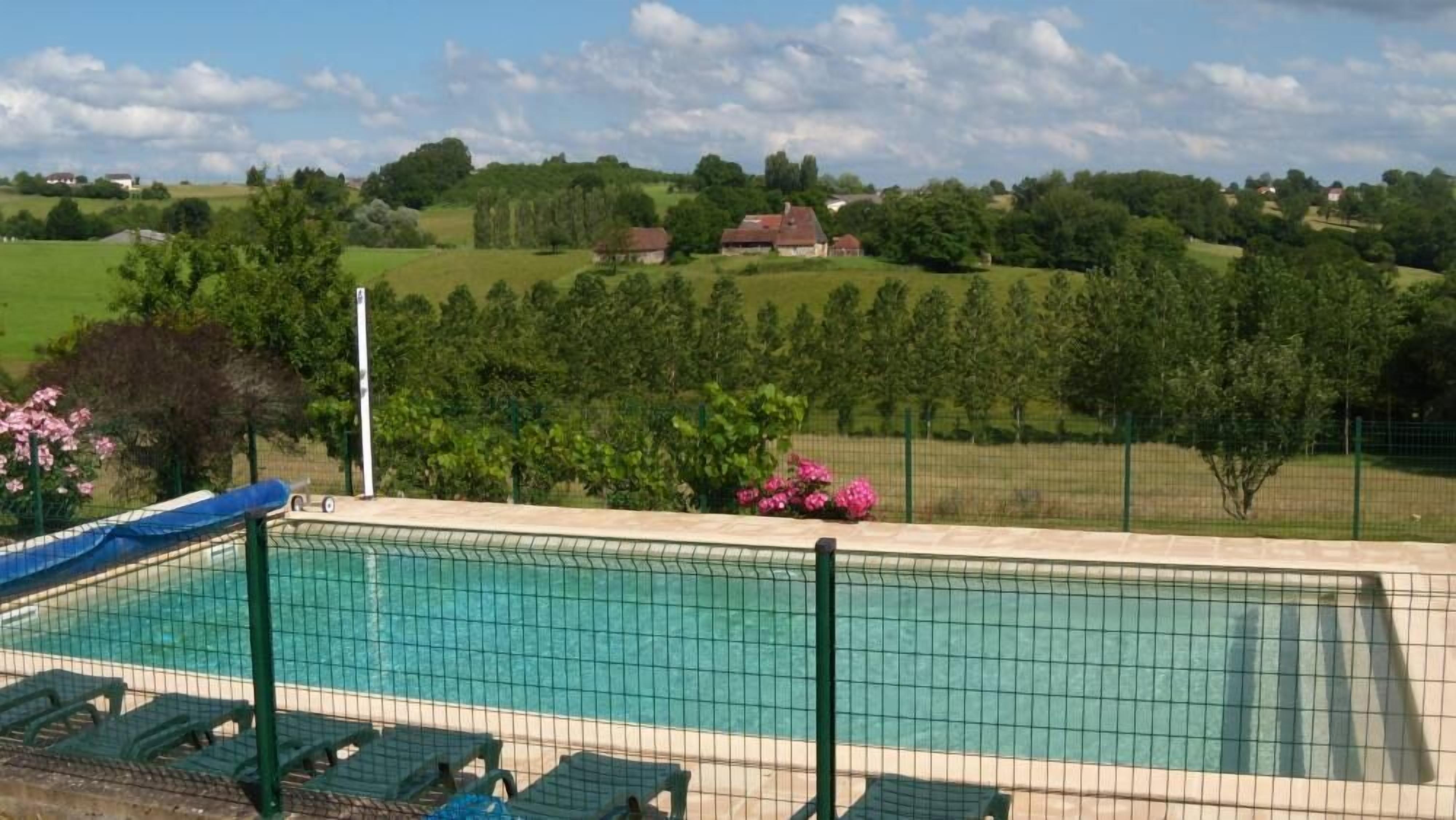 A swimming pool with a fence, surrounded by greenery and houses in the background.