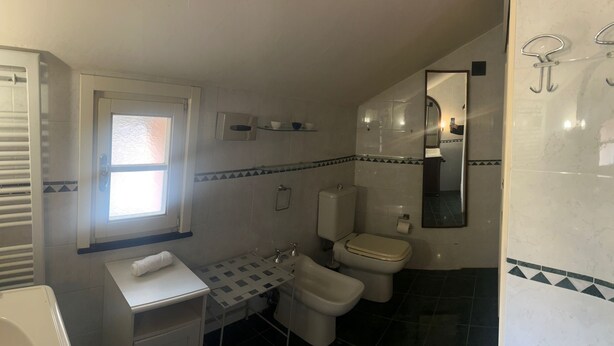 A bathroom with a toilet, bidet, sink, and a window.