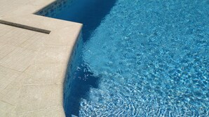 Een zwembad met helderblauw water, betegelde randen en een terras met ligstoelen.