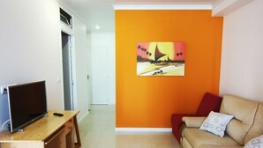 Een woonkamer met een houten bureau, een beige bank en een kleurrijk schilderij aan de muur.