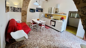 Una cocina acogedora con armarios blancos, una zona de comedor con un sofá rojo y un arco de piedra.