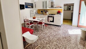 Una cocina moderna con armarios blancos, una zona de comedor con sillas rojas y un piso de terrazo.