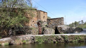 Ein Steinhaus mit Wasserrad und Steinmauer.