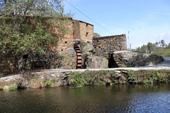 Un edificio de piedra con una rueda hidráulica y un muro de piedra.