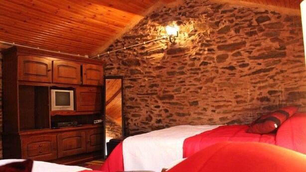 Ein Schlafzimmer mit Steinsandsteinwand, Holzbalkendecke und einem Bett mit roter Bettwäsche.