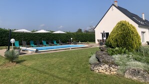 A swimming pool with lounge chairs and umbrellas, surrounded by a well-maintained lawn and a house with a sloped roof.
