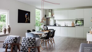 Eine moderne Küche mit weißen Schränken, ein Essbereich mit einem Holztisch und -stühlen sowie ein großes Fenster mit Blick auf Grünflächen.