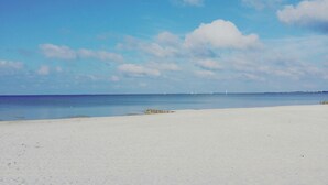 Ein weiter Sandstrand mit ruhigem Wasser und blauem Himmel.
