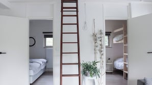 Ein Zimmer mit einer Holzleiter, einem Bett, einem kleinen Tisch mit einer Pflanze und einem Etagenbett.