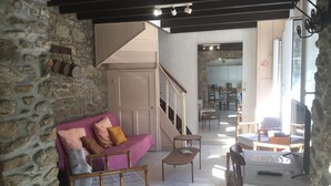 A cozy living room with a stone wall, a wooden sofa, a wooden chair, a small table, and a television. - DINARD VACATION RENTAL HOUSE (Dinard)